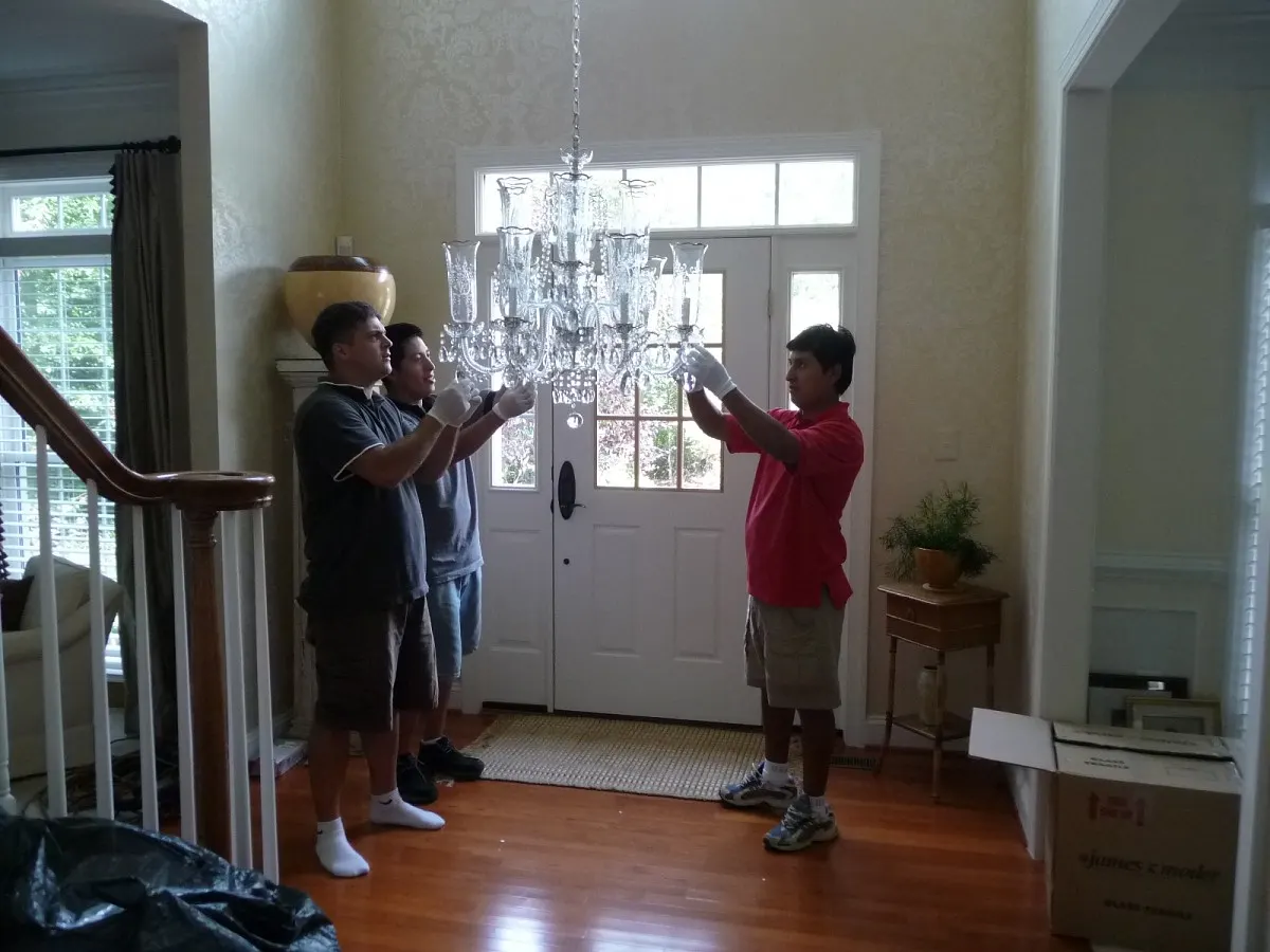 Three Current Power electricians hanging a crystal chandelier in a two-story foyer