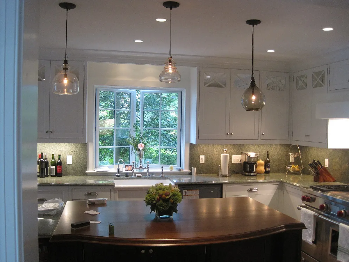 Renovated white kitchen with glass pendant lights over a dark island