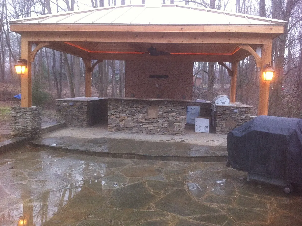 Outdoor kitchen pavilion with stone counters and lighting at dusk