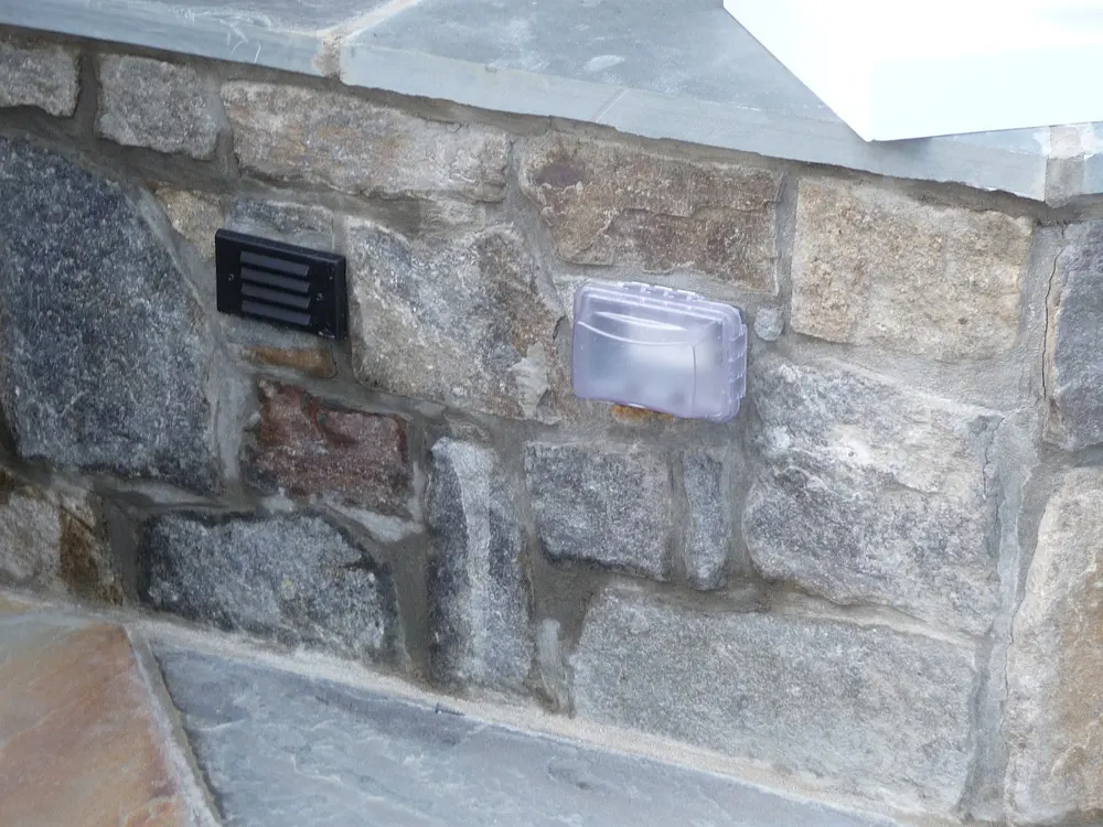 Stone wall with a built-in weatherproof outlet and a low-voltage step light